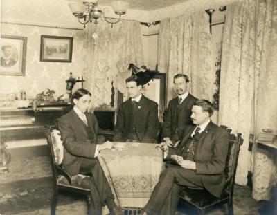 Portrait of Young Men Seated and Standing at Parlor Table