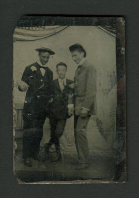 Photograph: Tintype portrait of three young men with flag in background, 1865 - 1875