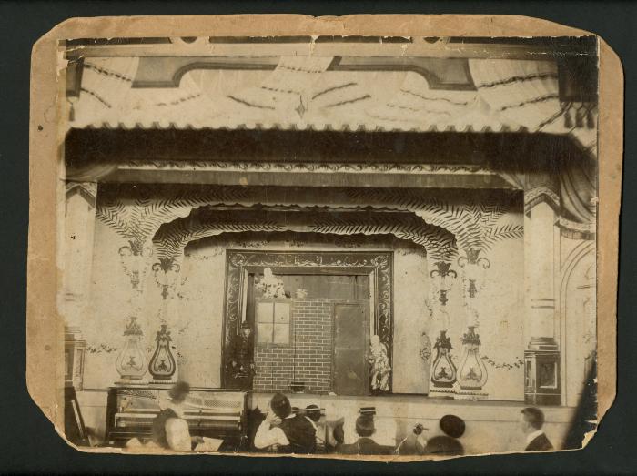 Photograph: View of stage in a music hall or theater, showing Trick House set and performers