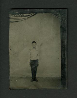 Photograph: Tintype portrait of a young boy with flag in background, circa 1870 